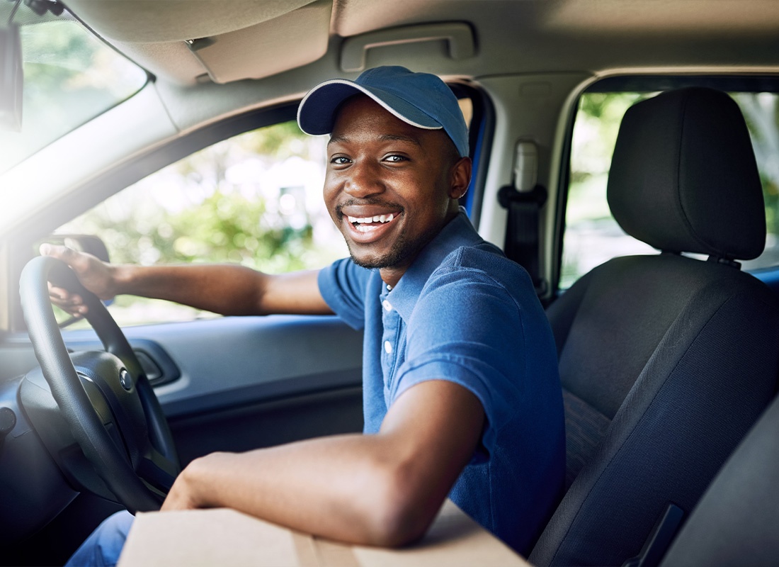Business Insurance - A Happy Male Delivery Driver Delivering Packages While Wearing a Blue Cap and a Blue Shirt